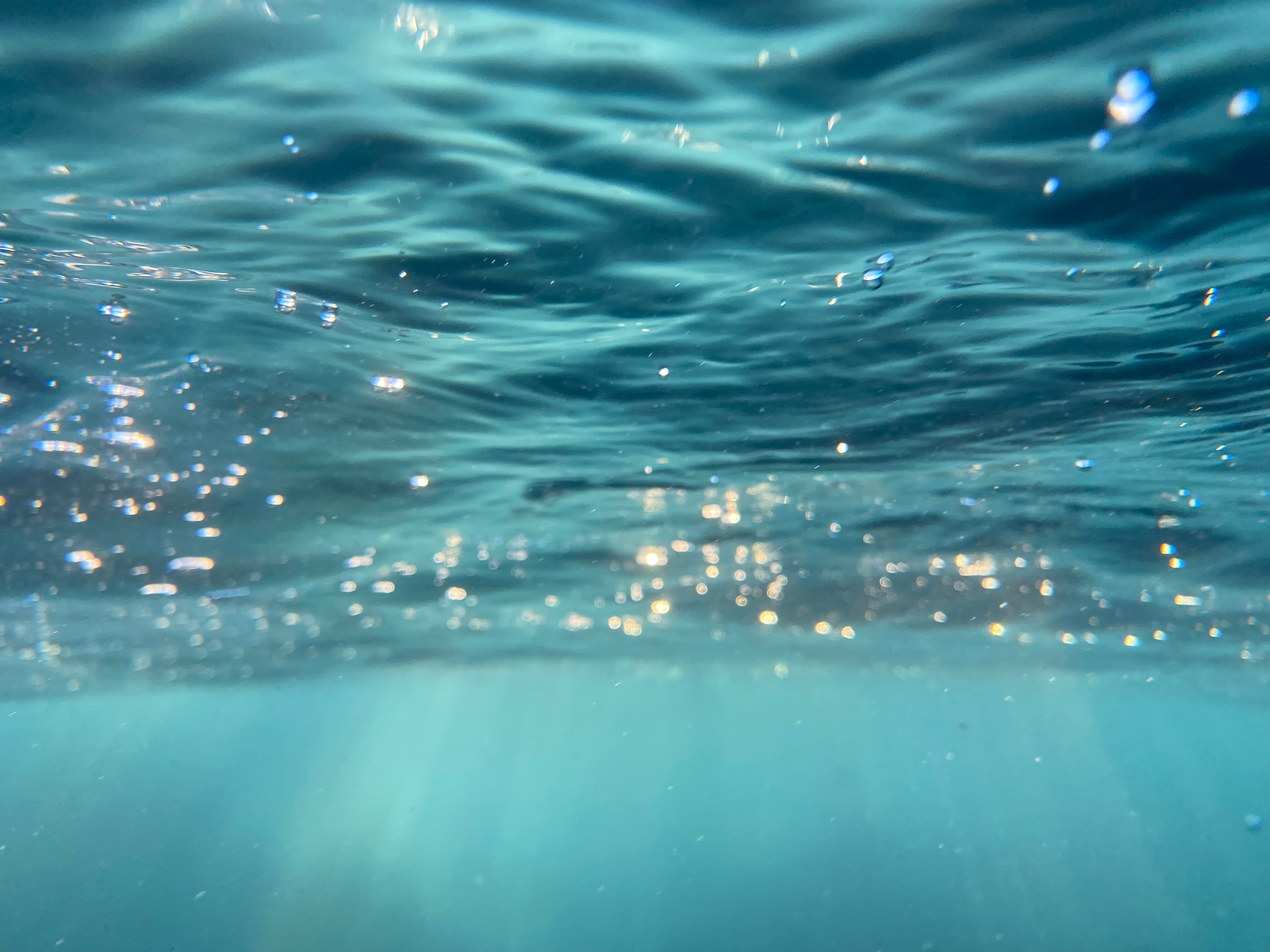 Underwater view of rippling blue water with sunlight reflecting off the surface and light filtering down into the clear turquoise water below.